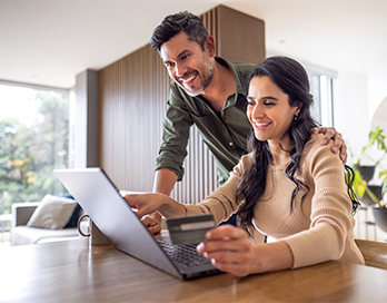 Young couple look at computer with debit card